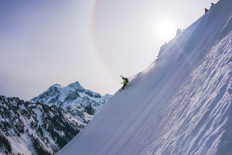 Another shot of a splitboarder making a big arching turn down a steep snowy face with Mount Shuksan in the background. 