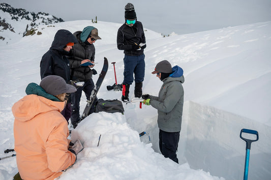 Lead guide and Founder of Guided Exposure shows a group of AIARE 1 students snow grains on a crystal card, during a snow pit lesson in the Mount Baker Backcountry. 