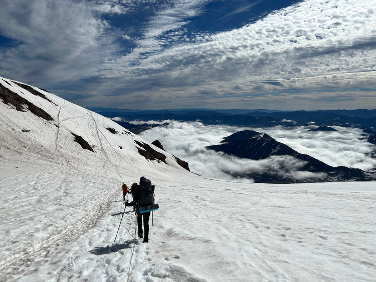 high and low clouds surround the mountains while the team descends on a rope during glacier travel