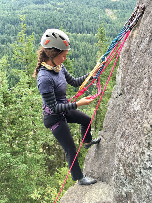A climber practices rock rescue systems while standing at a n anchor high above an emerald green forest 