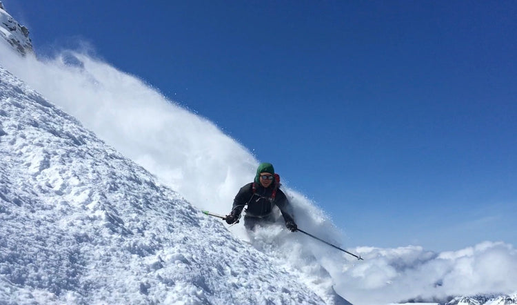 Skiing down a steep snowy face with a blue ski background. 