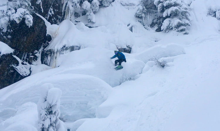 A snowboarder jumps of pillows of snow in the Mount Baker Backcountry during an advanced tour.