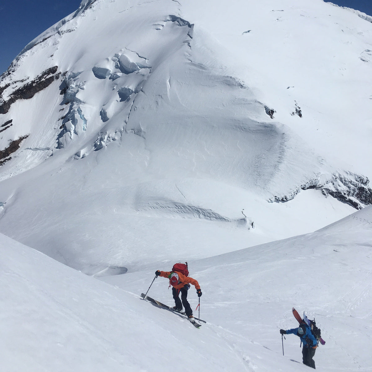 Mount Baker looms over a skier and snowboarder while ascending Colfax Peak. 