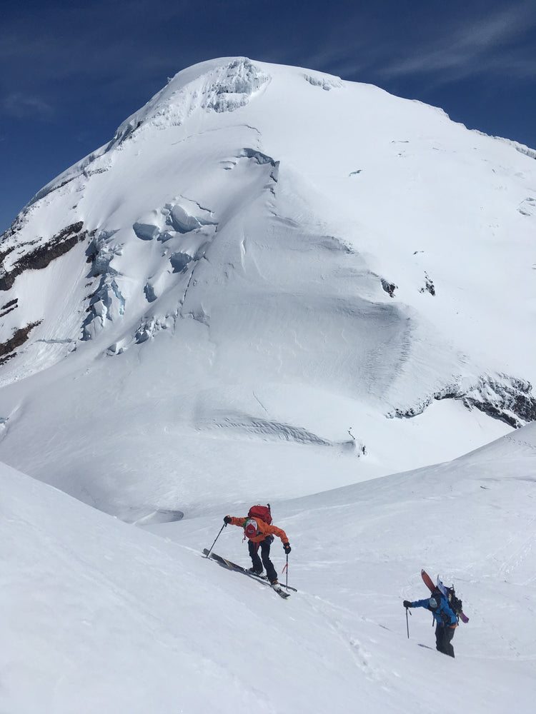 Mount Baker looms over a skier and snowboarder while ascending Colfax Peak. 