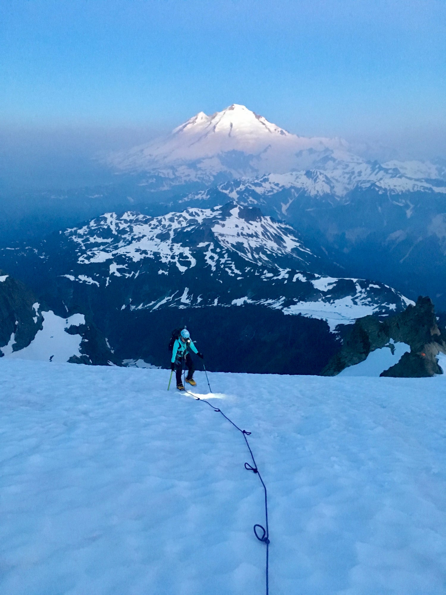 Walking up the sulphide glacier early in the morning, a light shadow of fog cloaks the lower mountains in the background, but Mount Baker rises above it. 