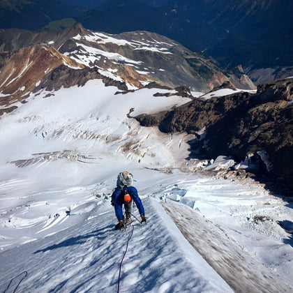 HIgh above the summer roosevelt glacier a climber ascends an exposed snow arete on Mount Baker North Ridge climb
