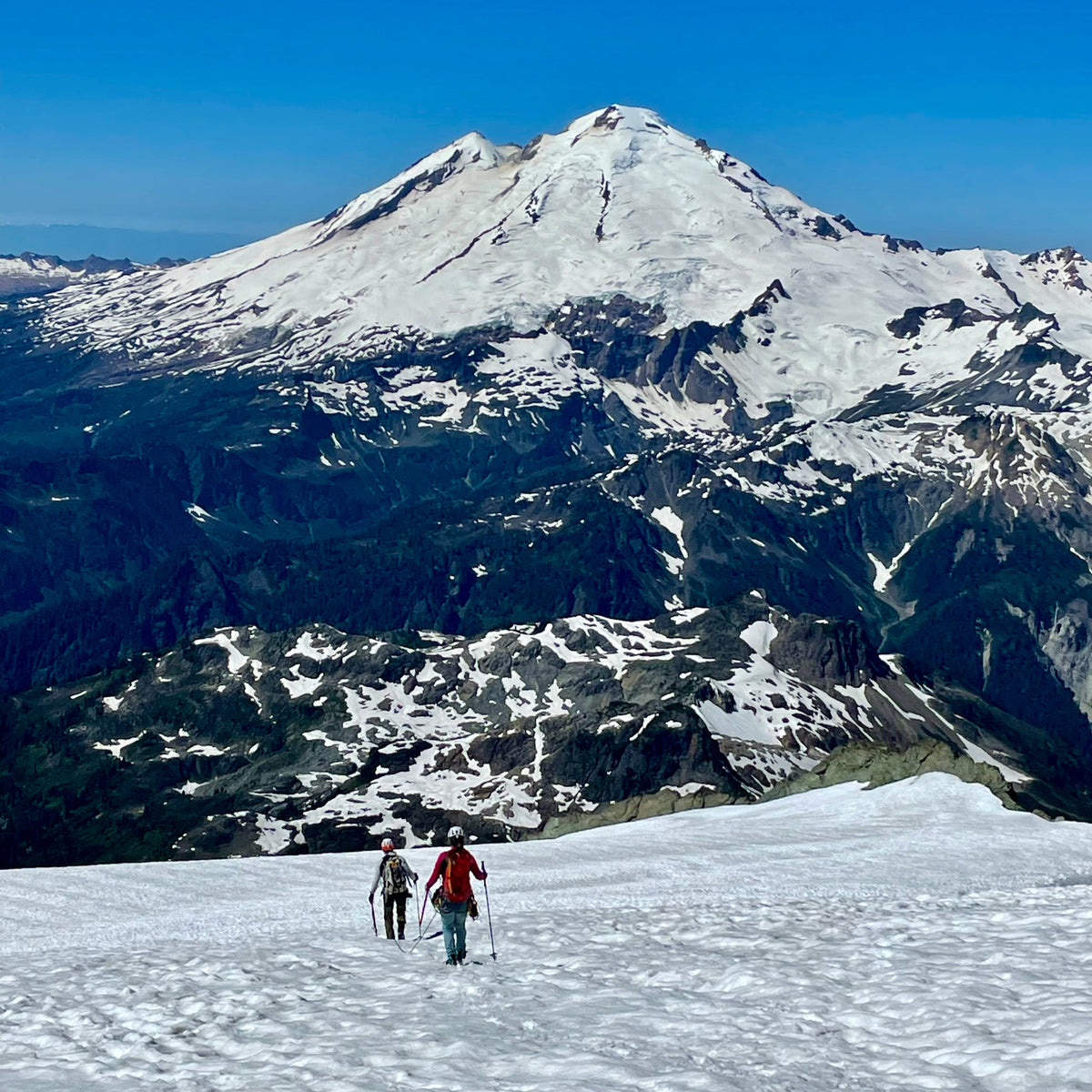 Climbers walking down the sulphide glacier after a successful summit of mount shuksan, with views of Mount Baker, park glacier, boulder glacier in the background.  