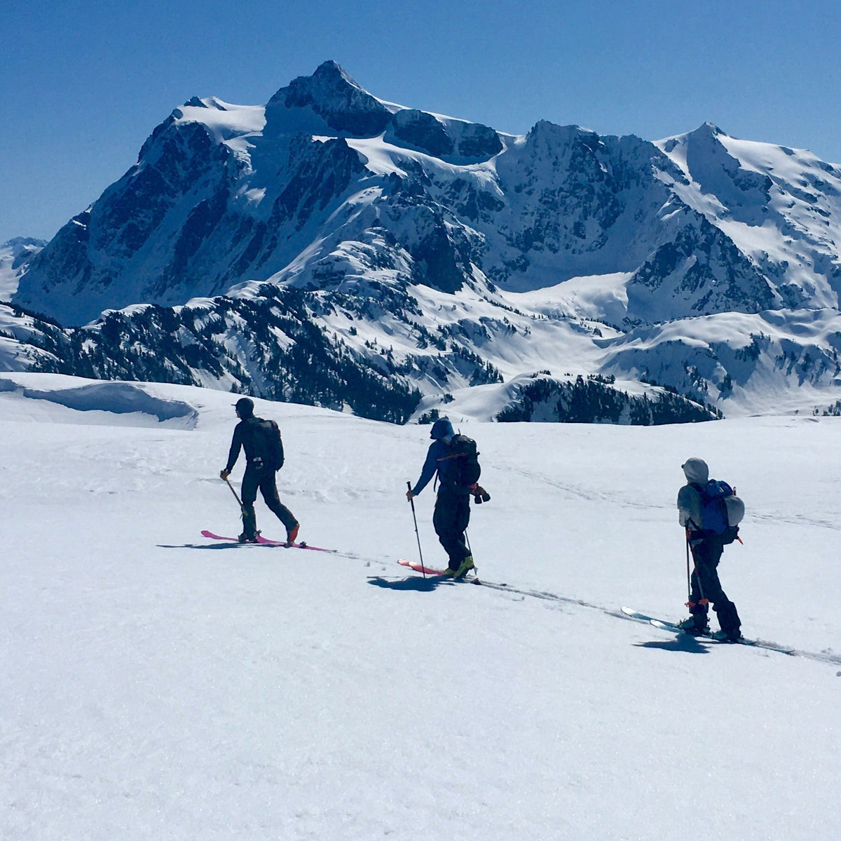 Three ski tourers skinning across an open glacier with Mount Shuksan behind during a 3-day splitboard and ski touring course